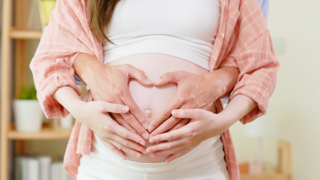 man holding wife's baby bump with heart-shaped hands